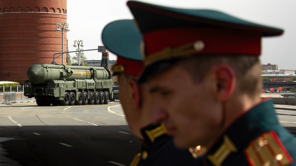 A color photograph of Russian soldiers in the foreground watching a ballistic missile being transported away in the distance.