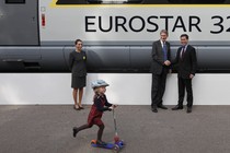 A girl rides a scooter past a commuter train