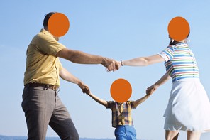 Two parents and one little kid hold hands in a circle, on a green field with a big blue sky in the background
