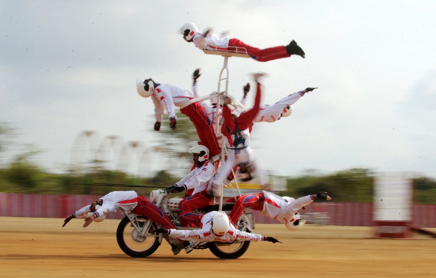 Ten stunt performers are strapped to a motorcycle with special rigging.