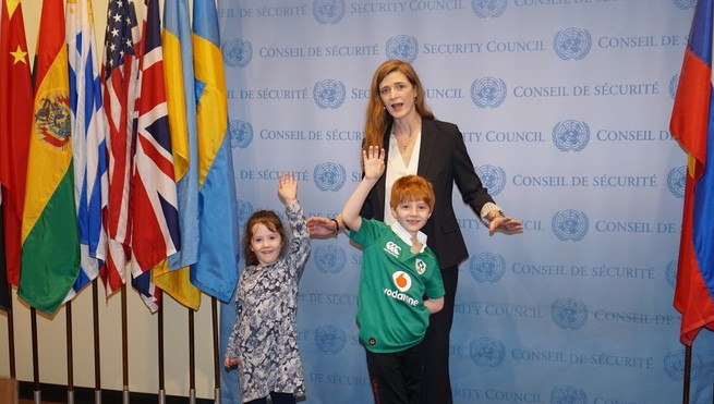 Samantha Power stands with her two children in front of flags and a security council banner