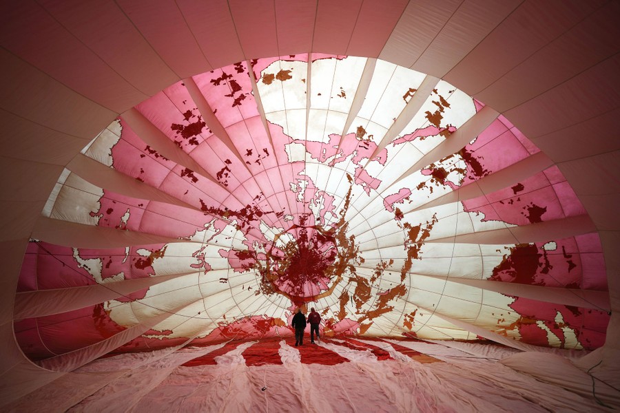 Two people stand inside a huge partially inflated balloon.