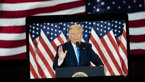 A TV image of former President Donald Trump speaking in front of U.S. flags