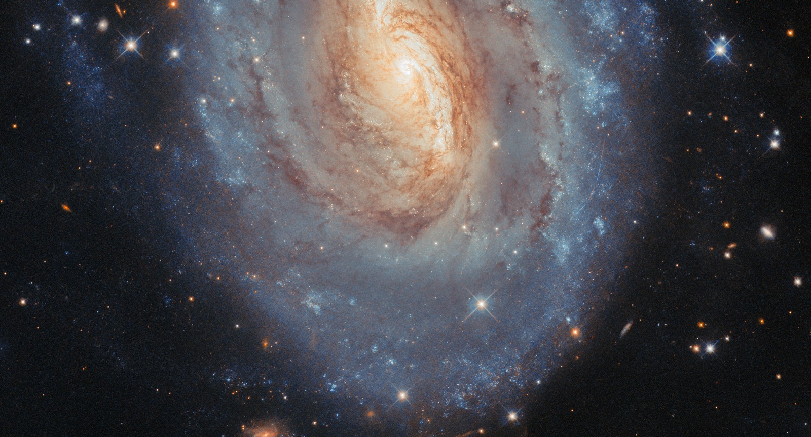 A telescopic view of a distant spiral galaxy with a yellowish center and more blue-colored star-forming regions toward the outer regions.