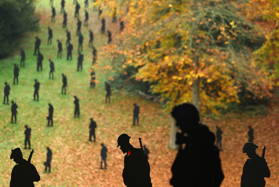 Dozens of cutout silhouettes of WWII-era soldiers stand in a park.