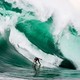 A surfer rides an enormous crashing wave.