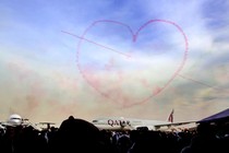 Pink smoke in the shape of a heart above an airplane