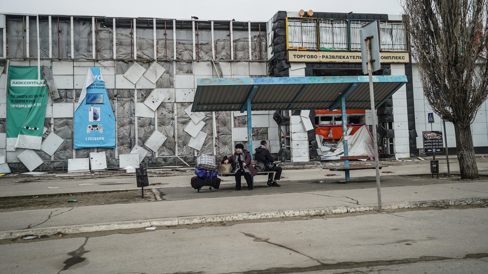 Two people sit at a bench in a Donbas town.