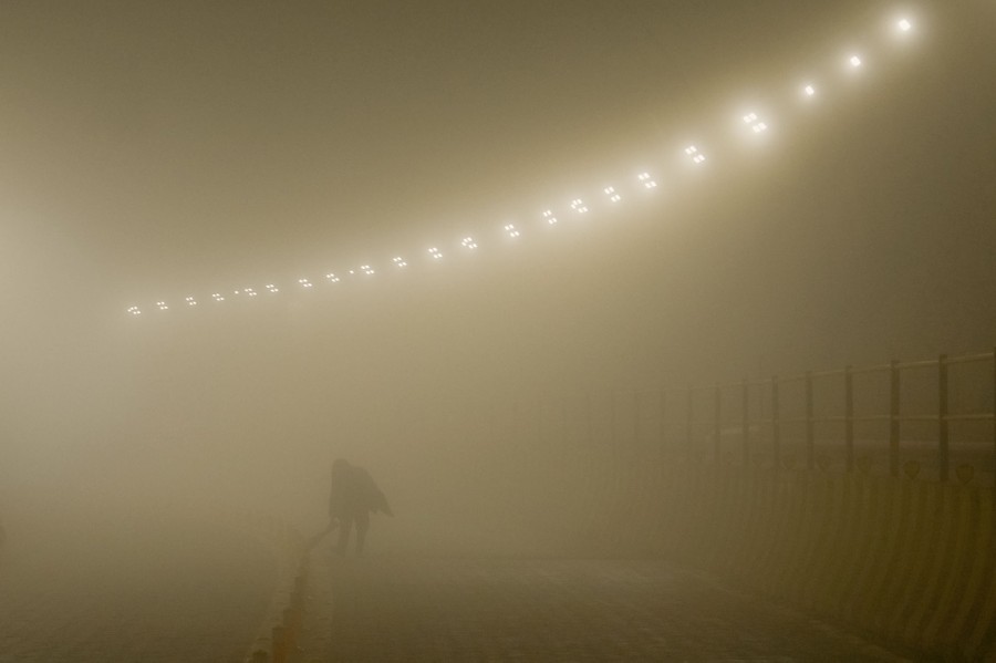 A worker cleans a road inside a dust-filled tunnel.