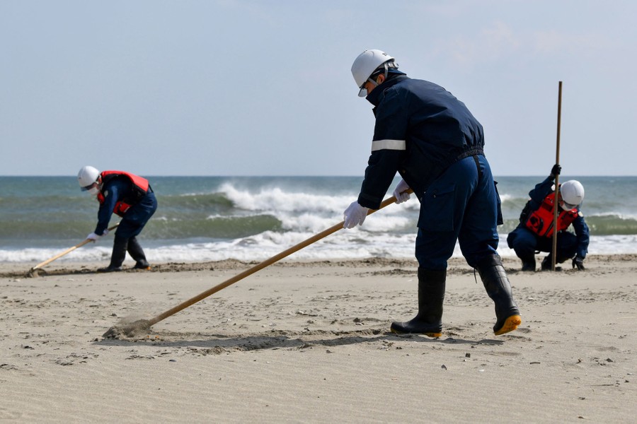 Three people work on a beach, examining the sand and using rakes.