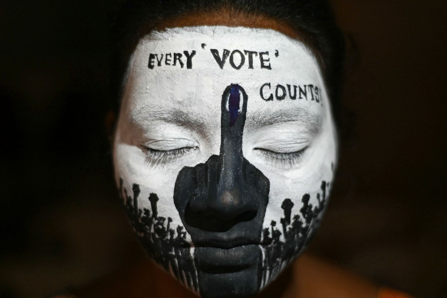 A demonstrator poses, showing their face covered in black and white makeup, depicting an upraised marked finger and the words "every 'vote' counts!"