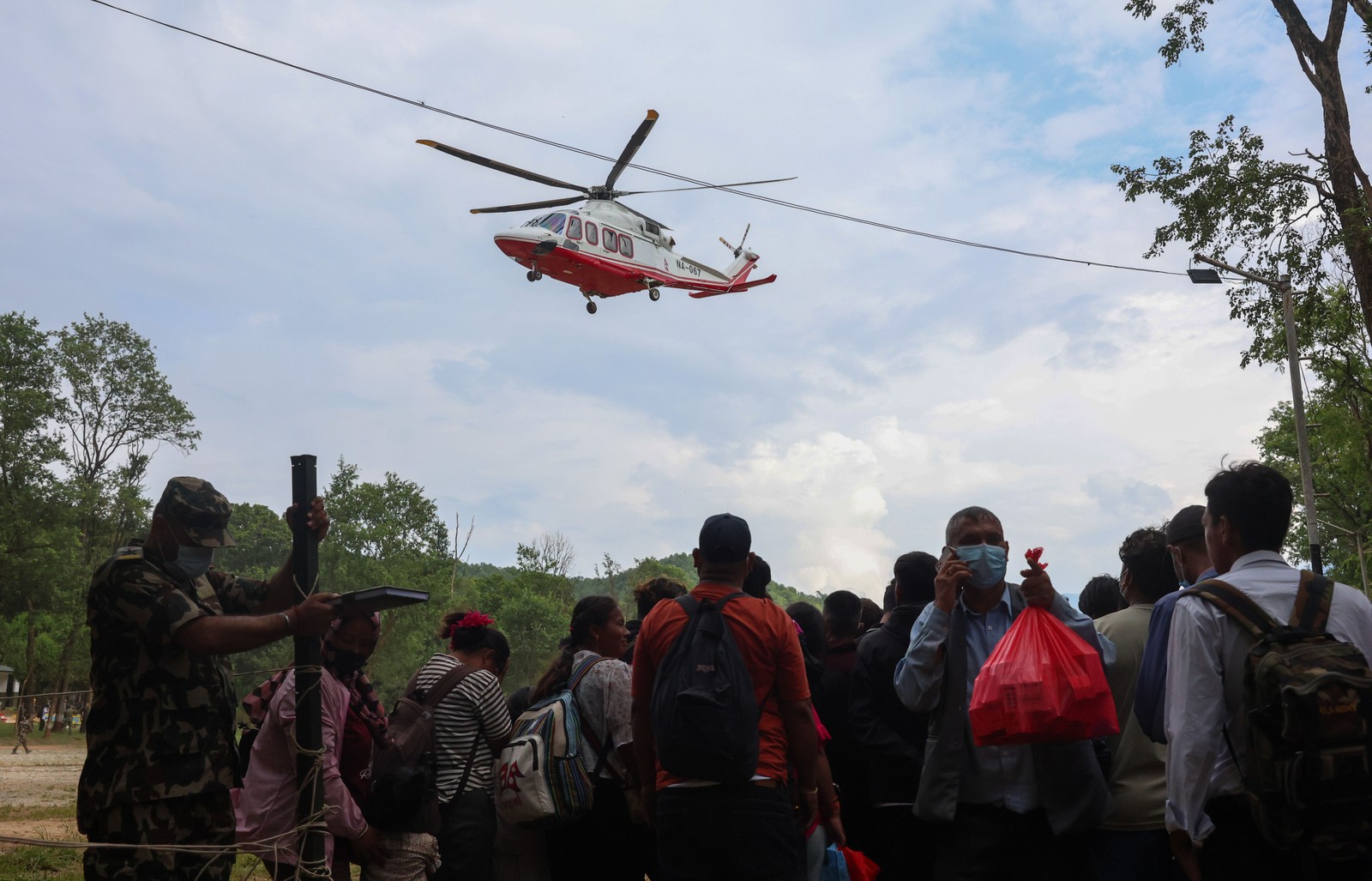 A rescue helicopter takes off from a clearing with a group of people nearby.