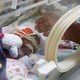 A hand reaches toward a premature infant in an incubator