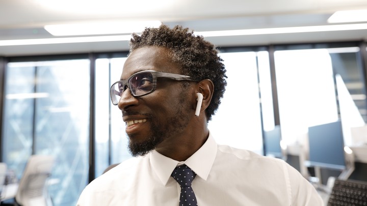 A man wearing Apple AirPod headphones smiles in an office