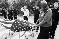 A man wheels the flag-covered body of a firefighter who died of COVID-19 past saluting officers.