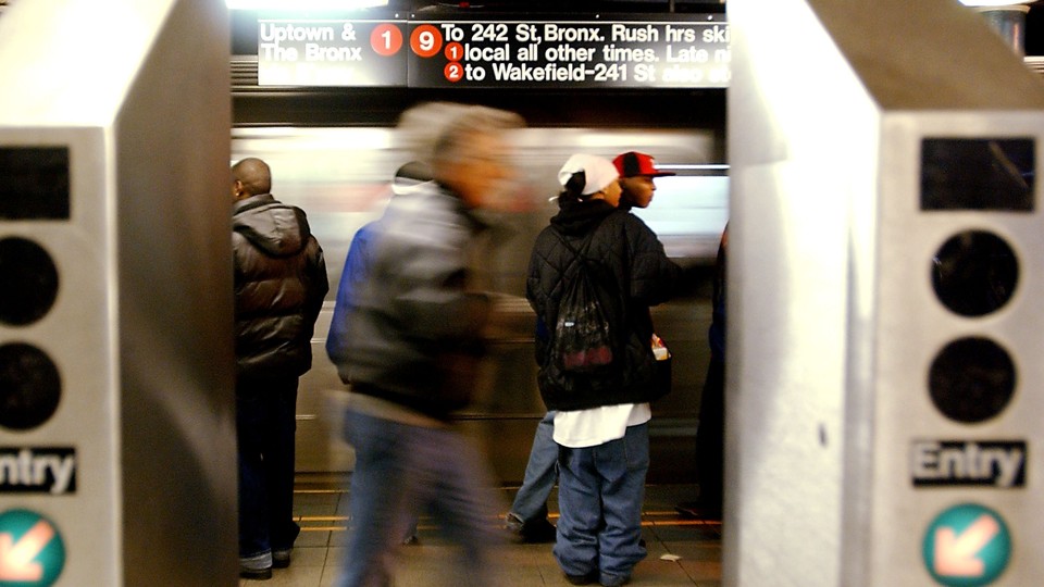 People standing on a subway platform in New York City, framed by two turnstiles