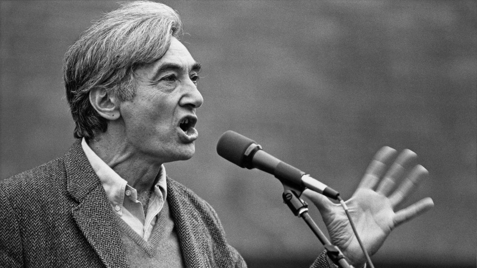 A man with gray, full hair speaking loudly into a microphone