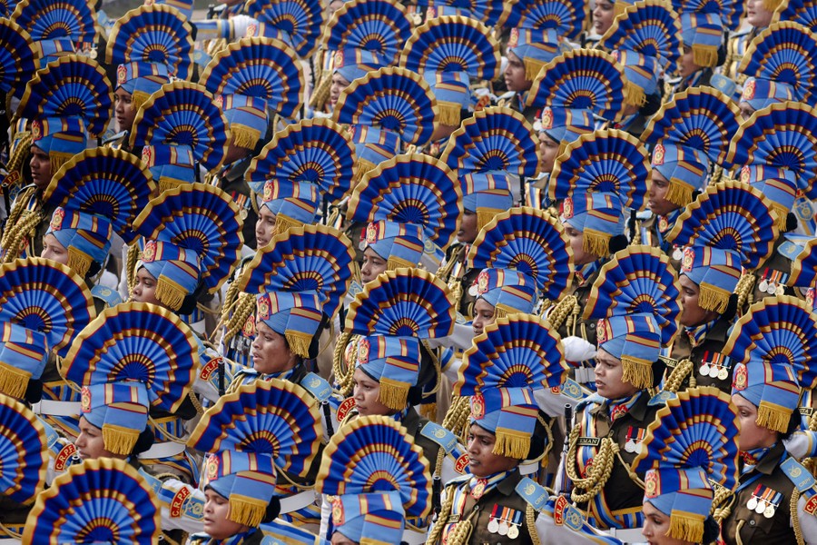 Rows of soldiers wearing dress uniforms and tall hats march in a parade.