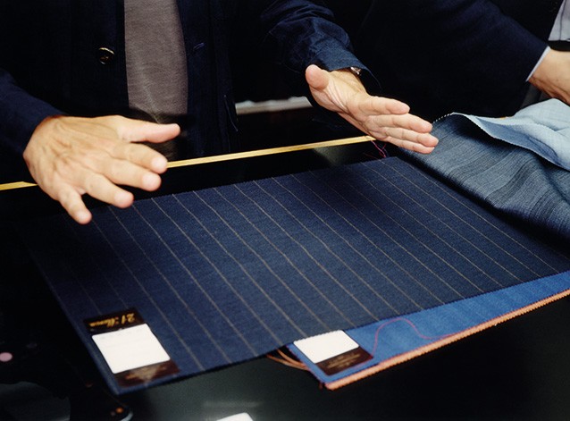 photo of the same two hands releasing the pinstripe navy fabric sample as it relaxes and lays flat without any wrinkles