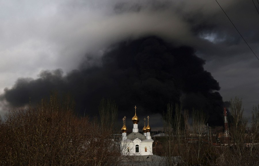 Black smoke rises from a fire in the distance with an Orthodox church in the foreground.