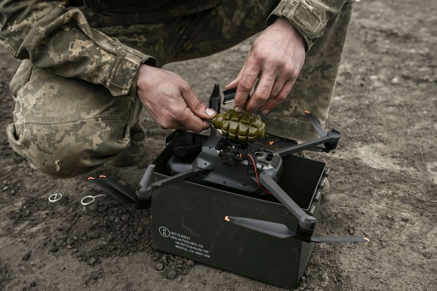 A soldier attaches a hand grenade to the underside of a drone.