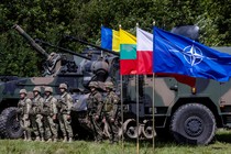 Soldiers stand next to tanks and the NATO flag