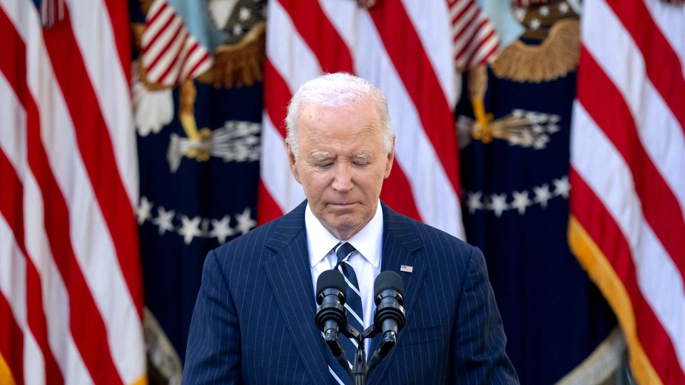 a photo of Joe Biden at a microphone, U.S. flags behind him, with his eyes closed