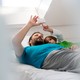 A father and son use an electronic device while lying in bed.