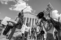 Black-and-white photo of anti-abortion protesters drumming and shouting through bullhorns in front of the Supreme Court, holding signs, including one that reads "Abortion PILLS are MURDER!"