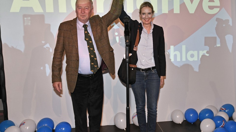 AfD top candidates Alexander Gauland and Alice Weidel hold hands in triumph in front of an AfD sign and balloons.