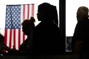 Voter are silhouetted near the American flag while voting in the California Statewide Special Election at the Huntington Beach Central Library in Huntington Beach Tuesday, Nov. 4, 2025.