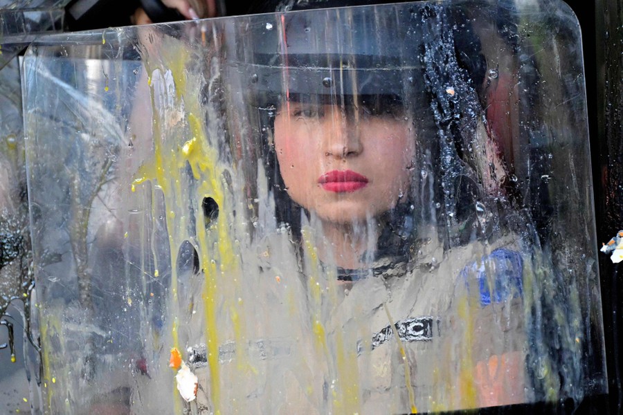 A police officer is seen standing behind a shield splattered with eggs.