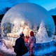 A parent and child stand in front of a blow-up snowglobe.