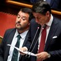 Matteo Salvini stares in dismay as Giuseppe Conte speaks at a podium.
