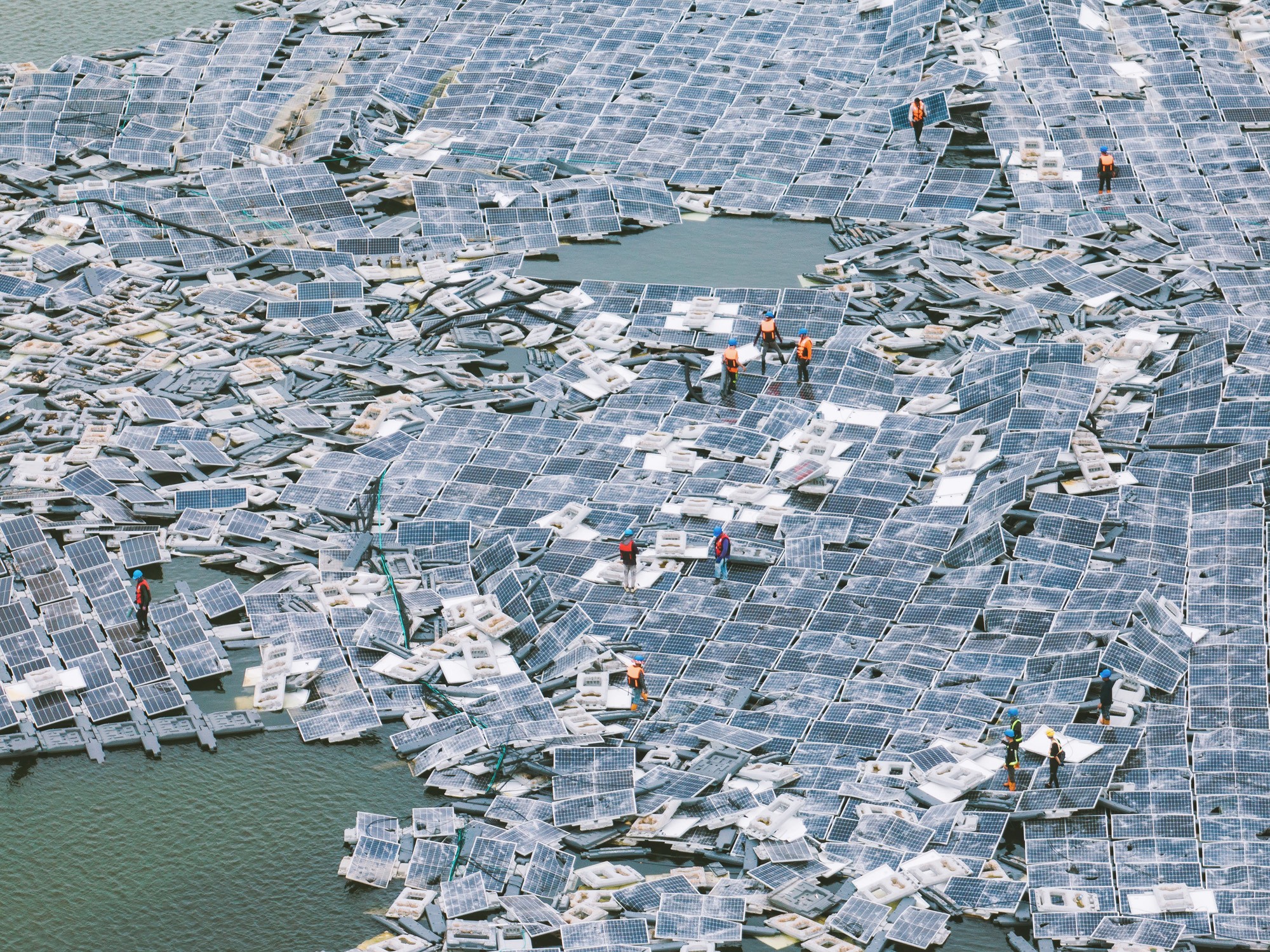 Several workers walk over a chaotic jumble of damaged floating solar panels.