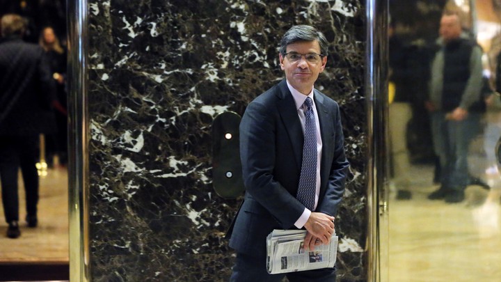 George Stephanopoulos stands in Trump tower and carries a newspaper.