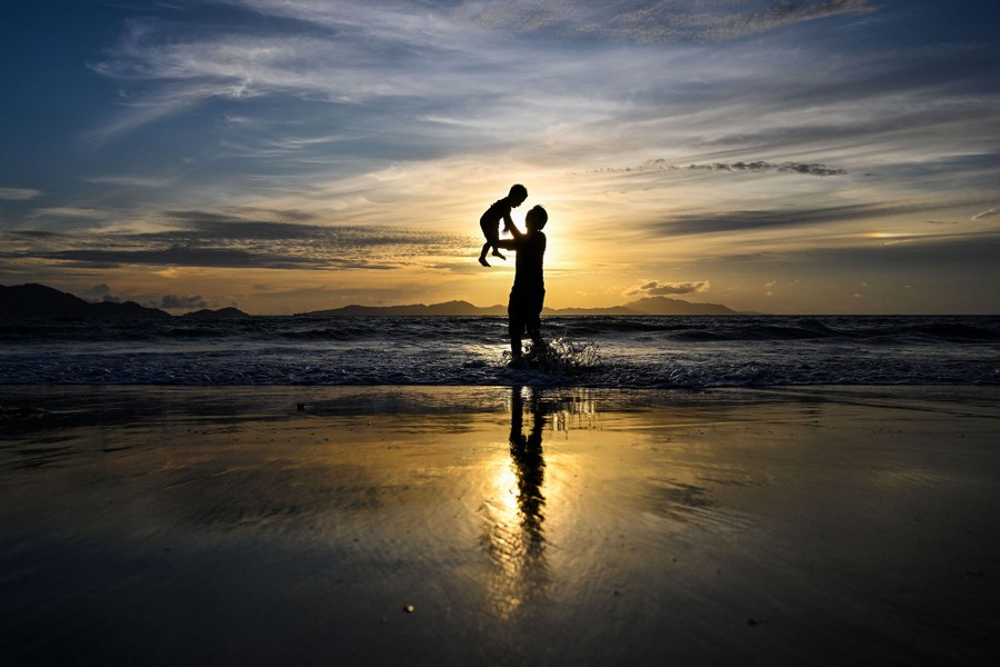 A man plays with his child at a beach at sunset.