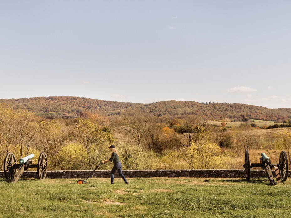 photo of the author using hand mower to mow grass between two Civil-War-era cannons on battlefield with hill in distance