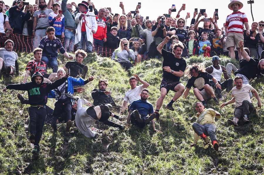 Onlookers cheer at the top of a steep hill as a group of runners begins a downhill race.