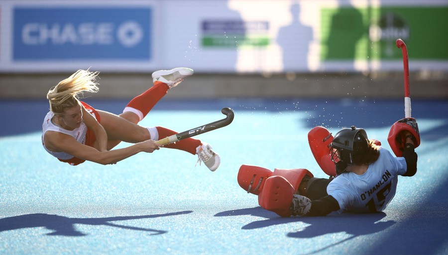 A field-hockey player dives as she makes a penalty shot, right in front of the goalkeeper.