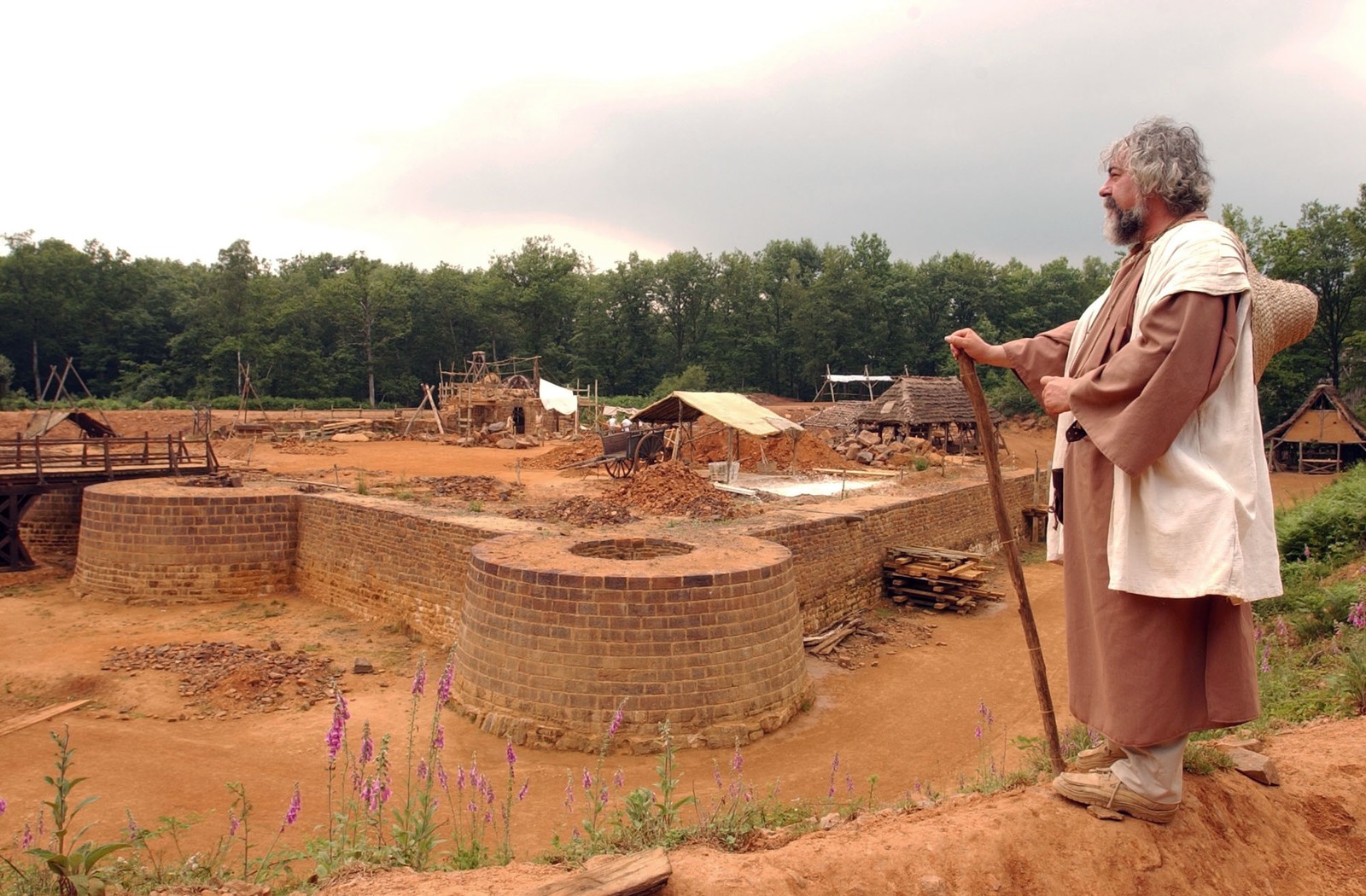 A person in medieval clothing stands at the building site of a castle.