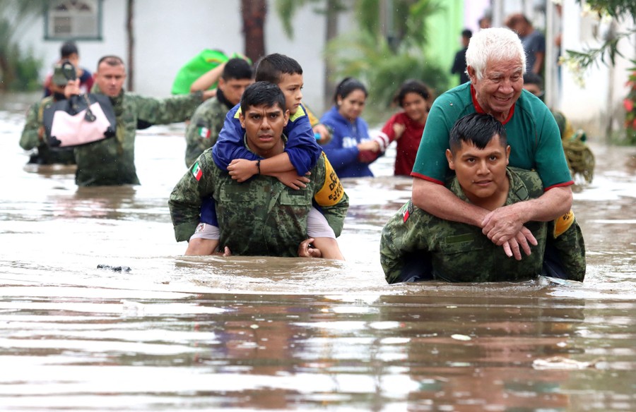 Members of the Mexican army carry people through chest-deep floodwater.