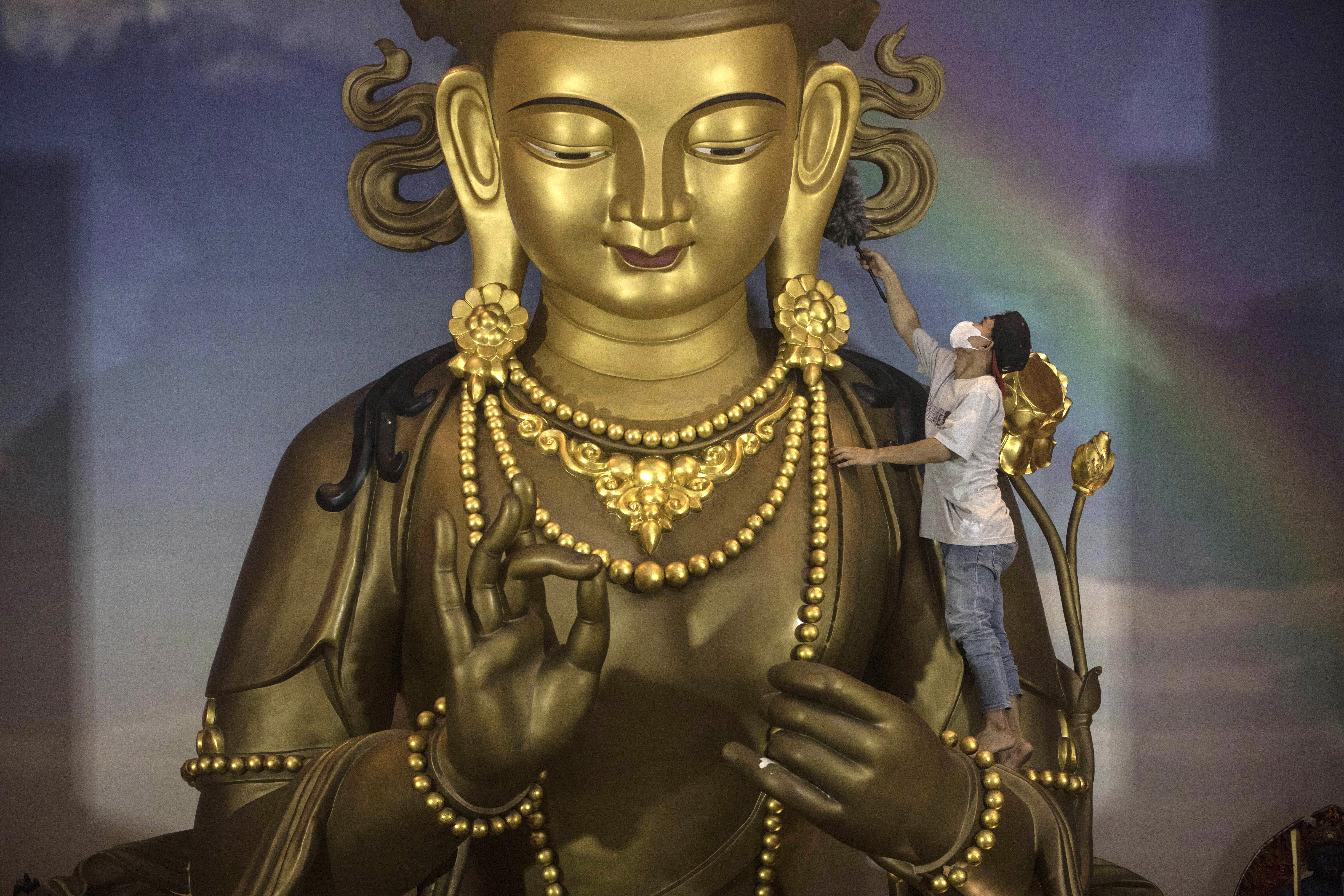 A worker cleans a large golden Buddha statue.