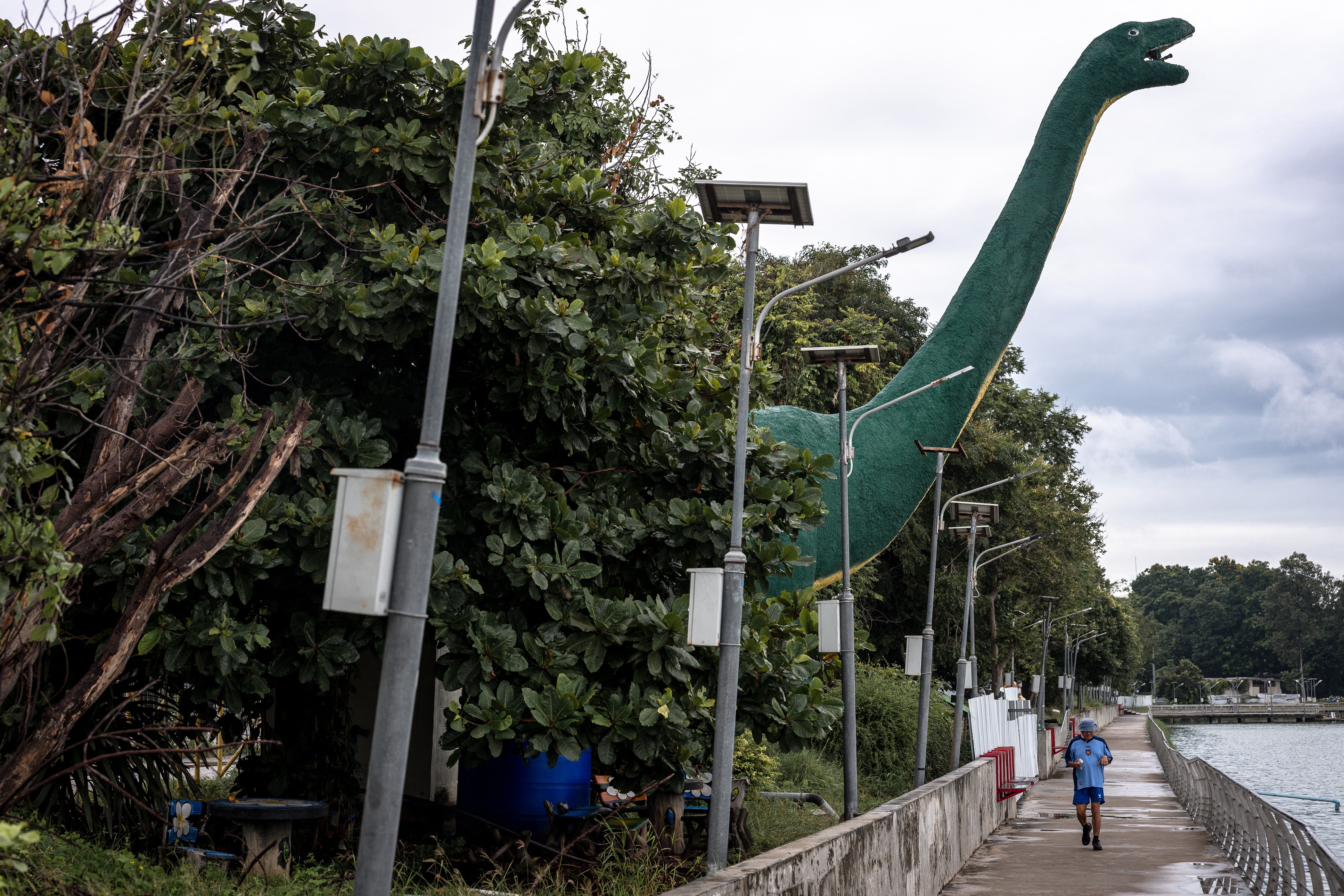 A man jogs past a tall dinosaur statue.