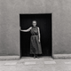 Two monochrome images of the same black doorway in an adobe wall, one showing O'Keeffe leaning on the frame, the other featuring Webb in the same stance