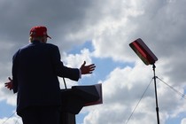 A photo of Trump speaking at a podium with the sky filling the frame