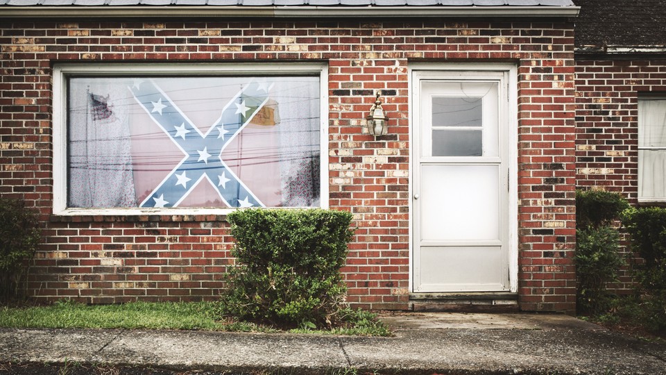 A Confederate flag hangs in the window of a house. 