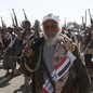 Houthi fighters march with weapons pointed in the air, a white-bearded militia member in the foreground.