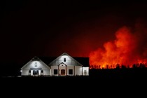 A nighttime view of a ranch house with a forest fire burning in the background