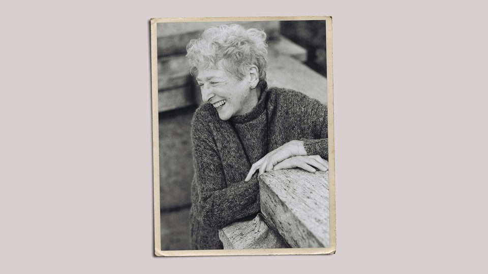 A woman with short gray hair in a gray sweater, laughing, in a photo with yellowed borders.